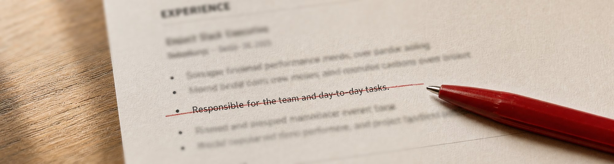 A printed CV on a desk. A red ballpoint pen has struck a line through the sentence "Responsible for the team and day-to-day tasks."